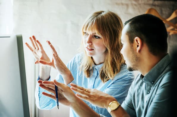 Female and male employee discussing project displayed on desktop screen
