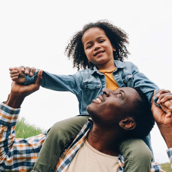 A toddler sits on her dad's shoulders.