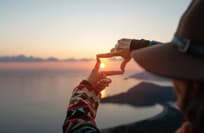 Woman makes finger frame on sea and islands at sunset