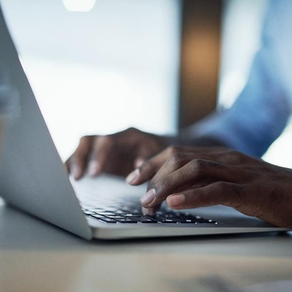 Closeup image of an African American person typing on their laptop keyboard