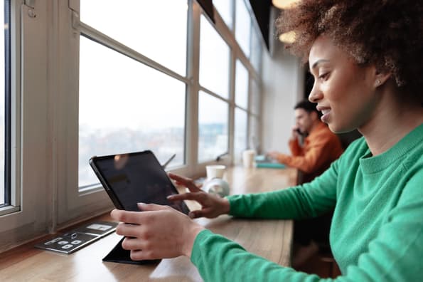 young woman sitting by the window of a coffee shop working on a tablet