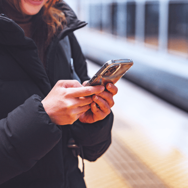 close up of a persons hands messaging on a cellphone while standing at a subway station