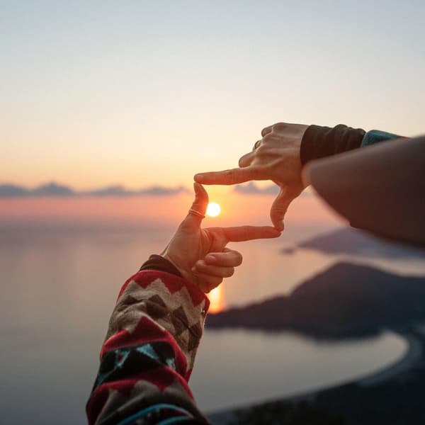 Woman makes finger frame on sea and islands at sunset