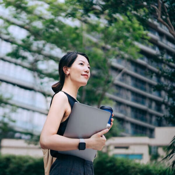 business woman standing in front of a tall building and holding a laptop
