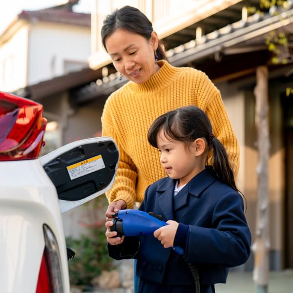 Young girl helping her mom to charge their electric car at home