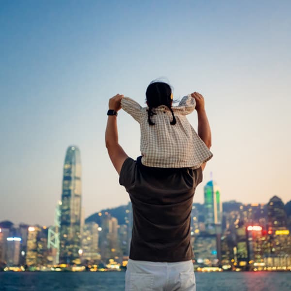 backside view of a father carrying his daughter on his shoulders while they look out at a large city in the distance