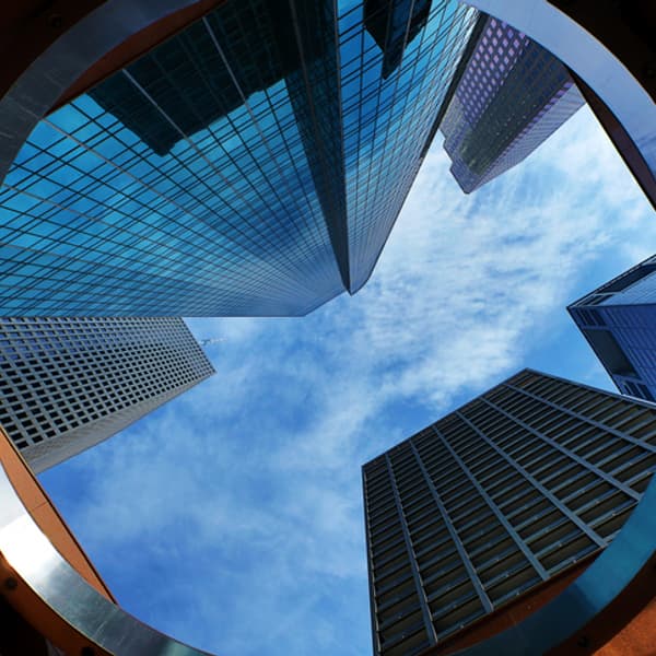 ground level view looking up at tall skyscrapers with a blue sky and clouds above the buildings