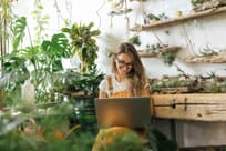Happy woman sitting in room with plants using laptop