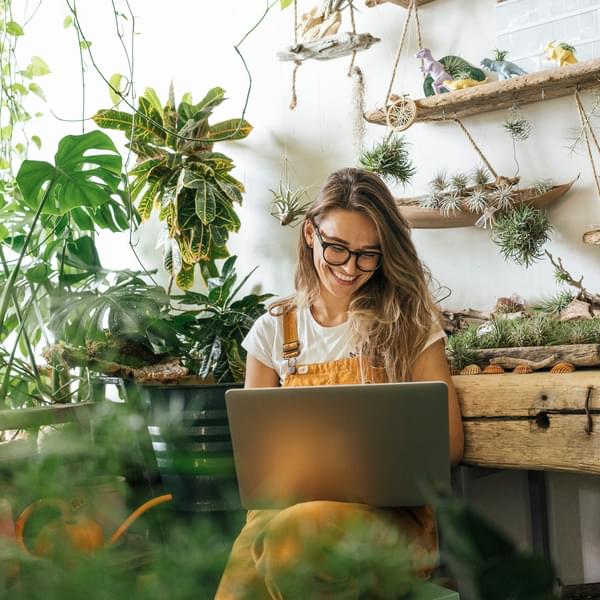 Happy woman sitting in room with plants using laptop