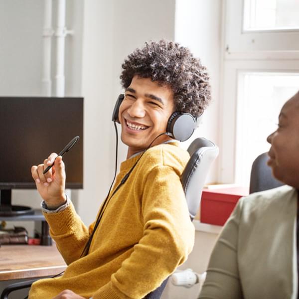 A happy and smiling young man sitting at a computer with headphones on
