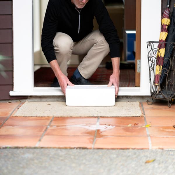 man bending down in the front doorway of his home to pick up a package that has been delivered on his doorstep