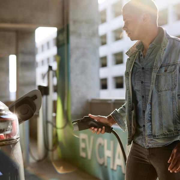 man at a charging station plugging in his electric vehicle to the charger
