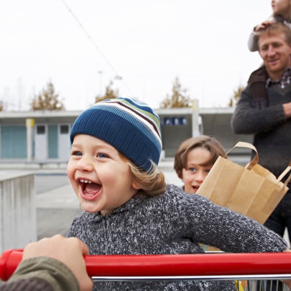 smiling toddler sitting in shopping cart being pushed by their parents