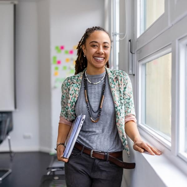 woman standing by the window of a classroom and smiling directly at the camera