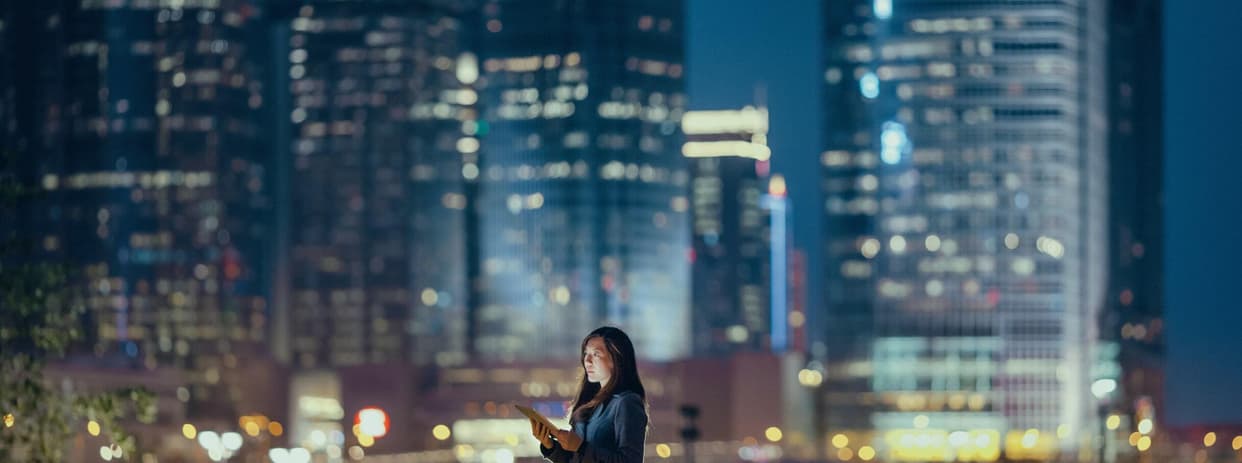 woman standing outside in a big city at night holding a tablet