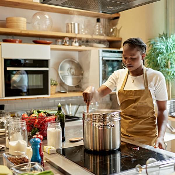 woman in a kitchen stirring a large pot of food cooking on the stovetop