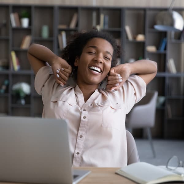 happy woman sitting at her desk stretching with her arms above her head