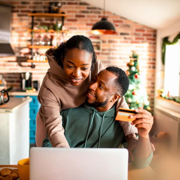 young couple sitting at their kitchen table with a computer and credit card shopping online