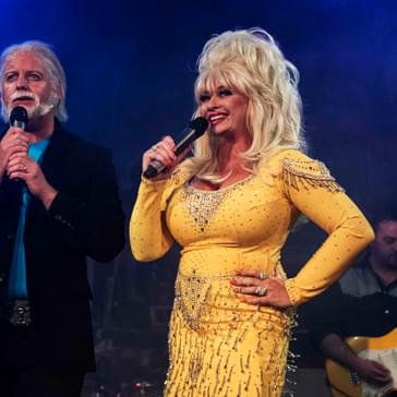 Performers impersonating Kenny Rogers and Dolly Parton stand singing on stage together