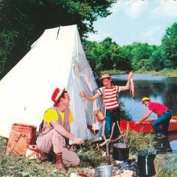 A family camp beside a river in the 1950s. They have a large tent and a boat. An adult cooks at a campfire.