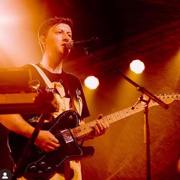 A stage shot of Pyramid Park, singing into a microphone and playing the guitar