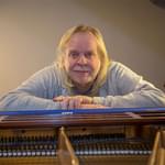 An image of Rick Wakeman leaning on a piano
