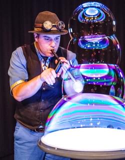 A man blowing through a straw to create a four-tiered bubble tower