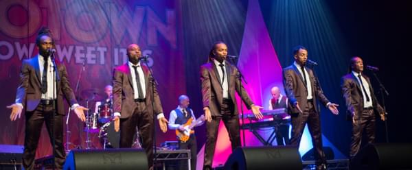 Five performers lifting their arms in unison on stage
