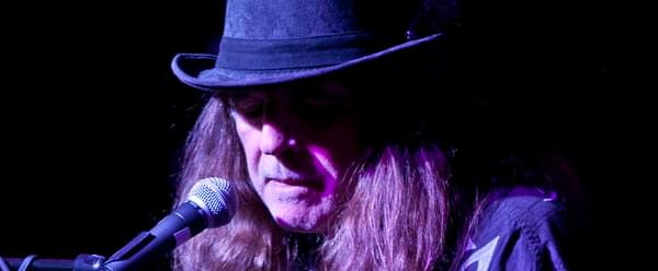 Claude Bourbon singing into a microphone whilst playing the guitar
