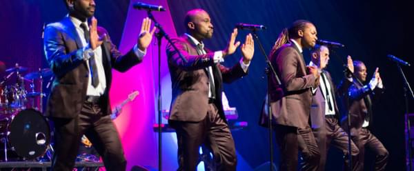 Five performers signing into microphones on stage