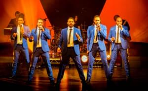 Five singers in blue suits performing on stage