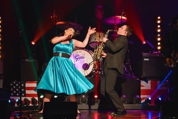 A woman in a bright dress sings to a man playing a saxophone