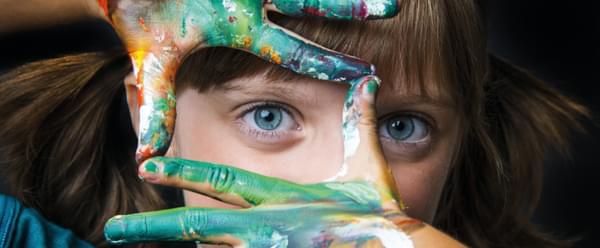 A child makes a frame with brightly painted hands and peers through