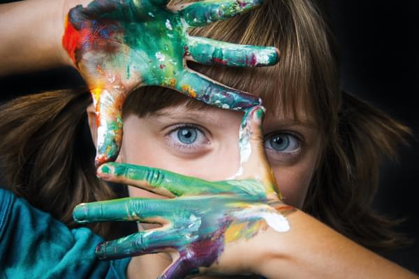 A child makes a frame with brightly painted hands and peers through