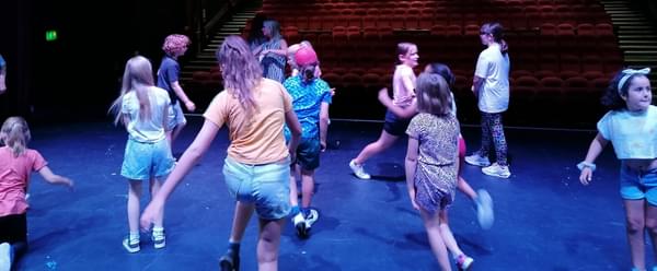 A group of young people dance around on a stage, facing out into the theatre's auditorium