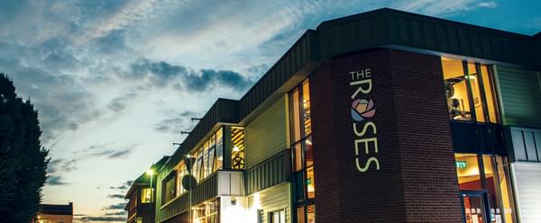 A view of The Roses' lit building against a striking dusky sky