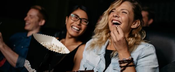 A row of smiling people laugh and eat popcorn whilst watching a film
