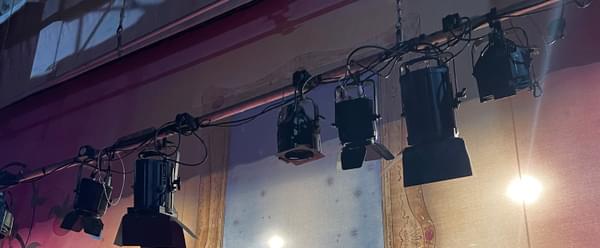 A theatre's lighting bars are lowered onto a stage, in front of a colourful pantomime backdrop