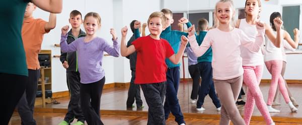 A group of primary aged boys and girls learn choreography in a studio