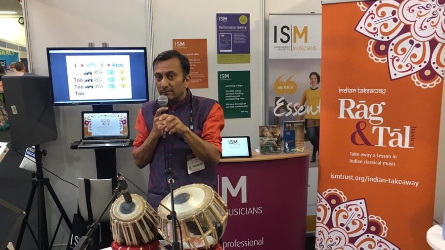 The resource creator, Head of Ealing Music Service Yogesh Dattani, standing in front of a Rag & Tal roller banner with a microphone in his hand.