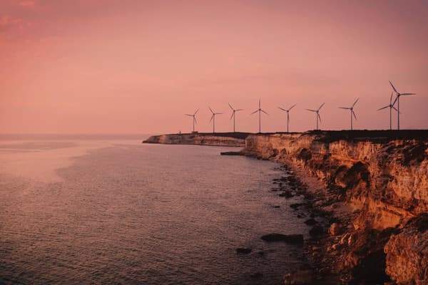 A scenic image of a cliff front lined with wind turbines overlooking the sea. The image has a sepia tone making it feel warm and nostalgic.
