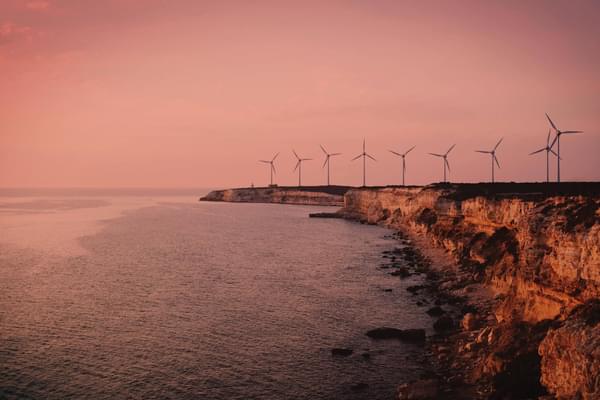 A scenic image of a cliff front lined with wind turbines overlooking the sea. The image has a sepia tone making it feel warm and nostalgic.