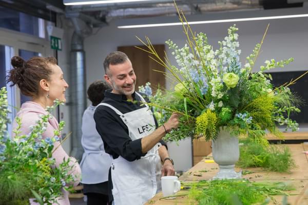 Teacher and student smiling at the vase bright and elaborate flower arrangement they are working on.