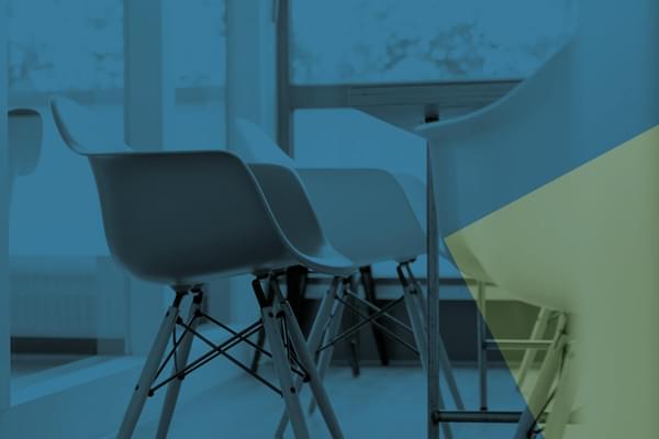 Stylised image of modern plastic bucket seats around a table. The image is tinted in a navy blue colour with an overlaying yellow triangle in the right corner of the image.