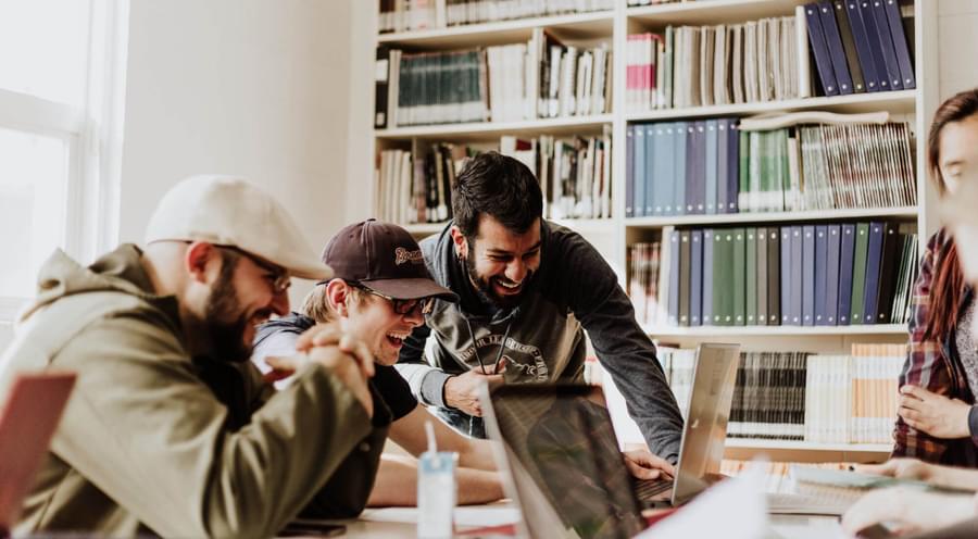 Men standing around a computer laughing.