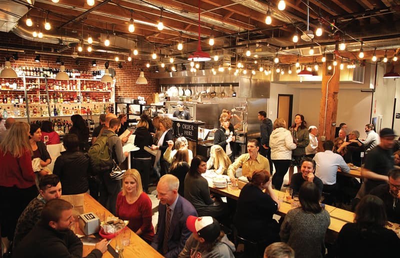 Many people eating at communal tables under festoon lighting