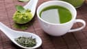 Eine Tasse mit Grünem Tee, daneben zwei Löffel mit Grünteepulver- und Blättern.