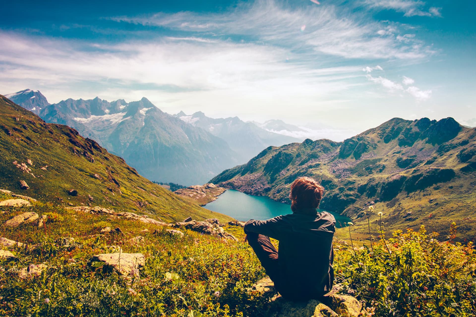 Ein Mann sitzt auf einem Berg und schaut auf einen See.