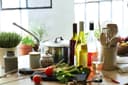 Verschiedene Weine stehen in Flaschen neben Töpfen und Gemüse in der Küche