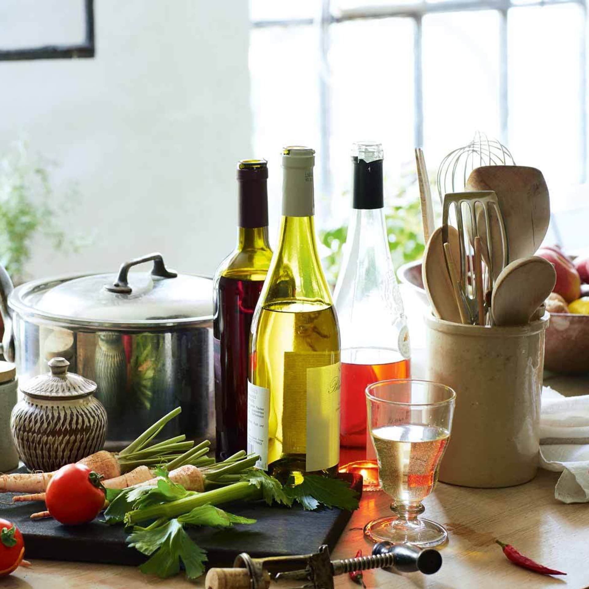 Verschiedene Weine stehen in Flaschen neben Töpfen und Gemüse in der Küche